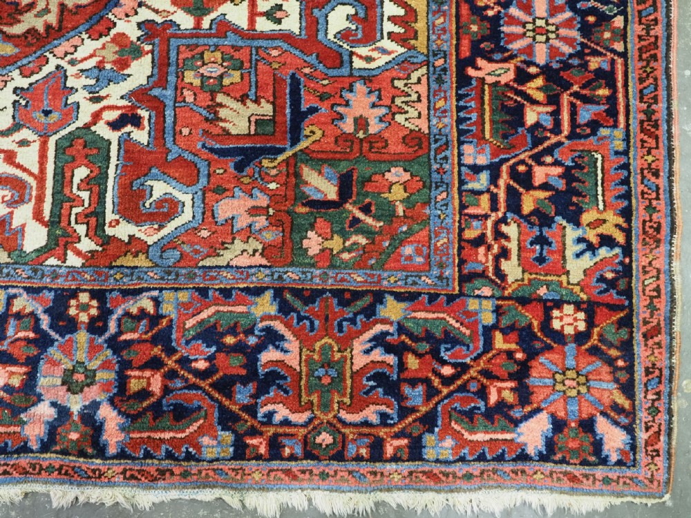 An antique hand-knotted Persian Heriz wool carpet featuring a central geometric medallion, angular spandrels, a terracotta red field, and navy blue borders. View XII