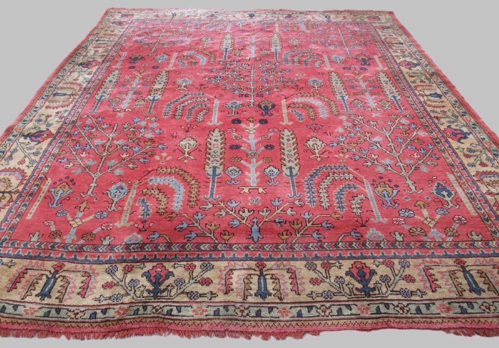 An antique Turkish Oushak wool carpet featuring a dominant pink ground decorated with stylized willow tree motifs and framed by a light beige floral border.
