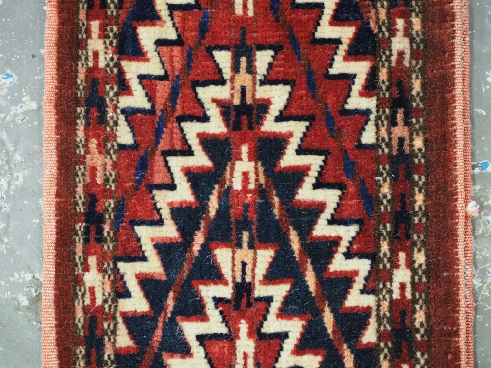 An antique handwoven Yomut Turkmen spindle bag face with geometric red, navy, and ivory serrated zigzag patterns. View IV