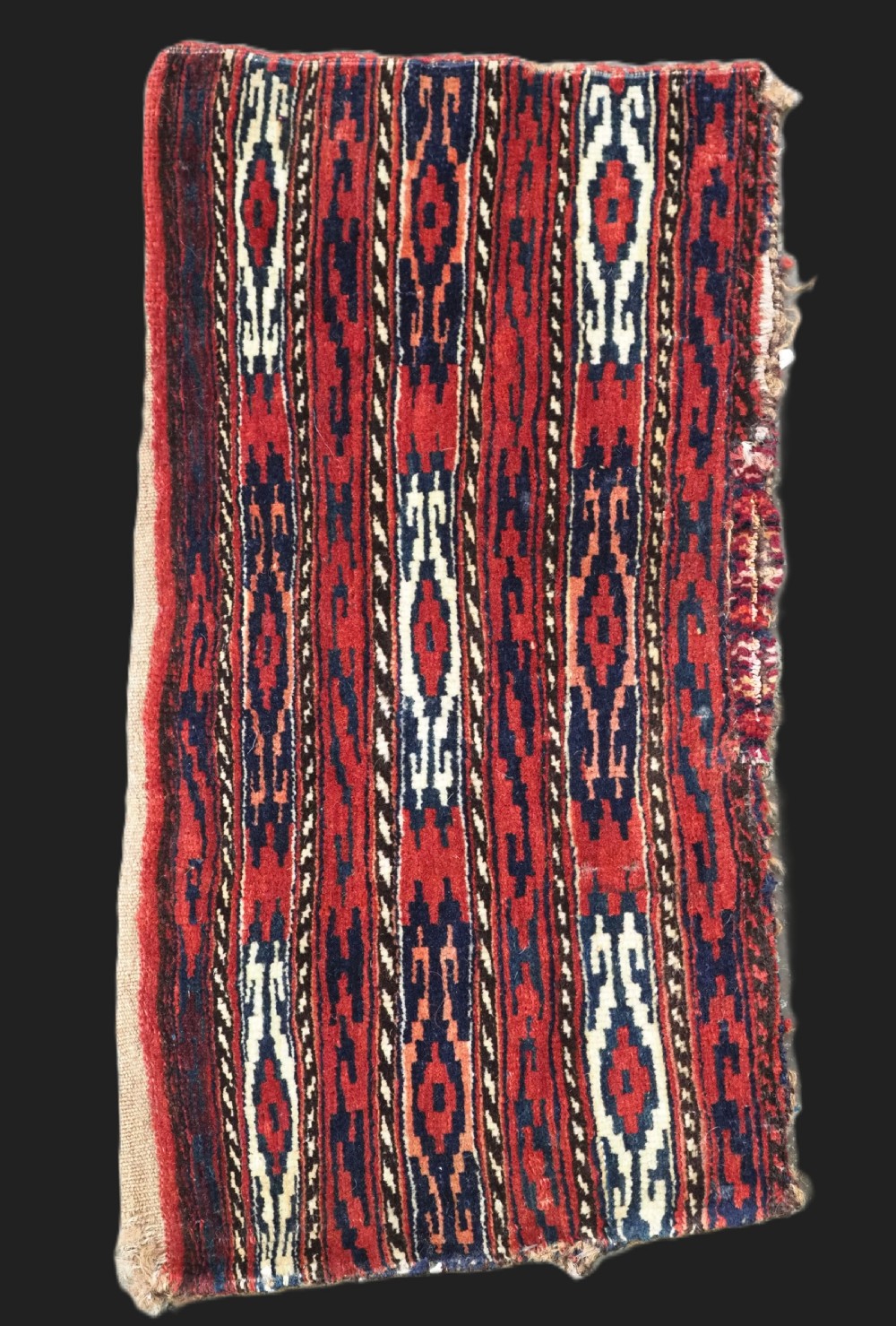 A vertical hand-woven wool Turkmen spindle bag featuring vertical geometric striped patterns in deep red, navy blue, and ivory tones.