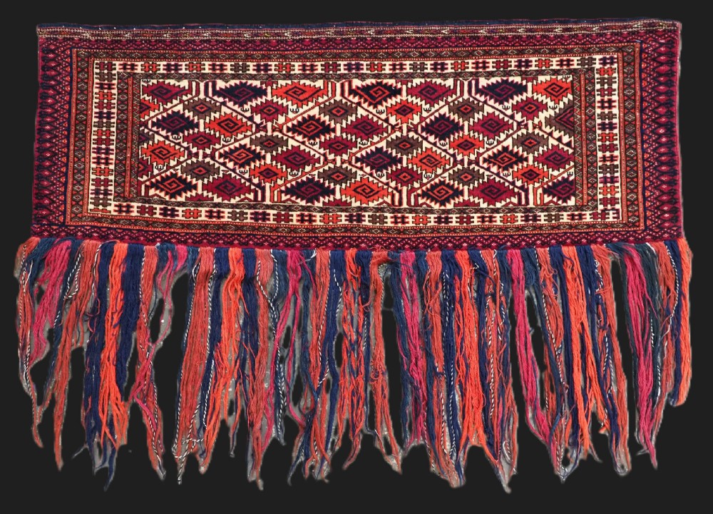 An antique rectangular Tekke Turkmen woven torba face featuring a geometric diamond lattice pattern in burgundy, cream, and orange, finished with long polychrome wool fringes along the lower edge.