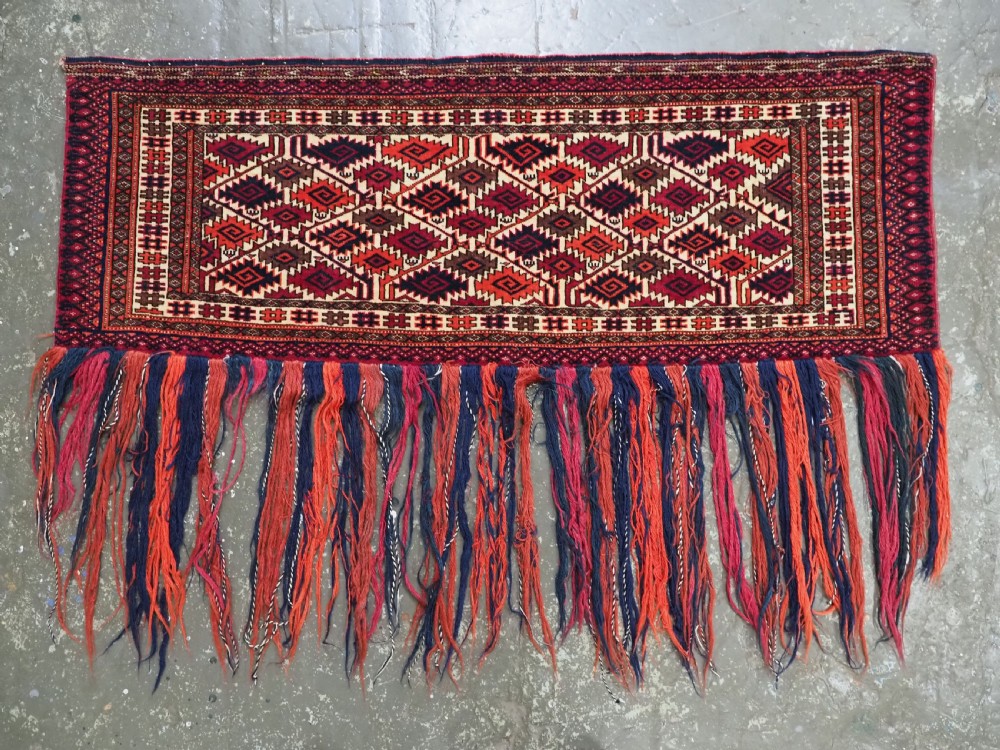 An antique rectangular Tekke Turkmen woven torba face featuring a geometric diamond lattice pattern in burgundy, cream, and orange, finished with long polychrome wool fringes along the lower edge. View II