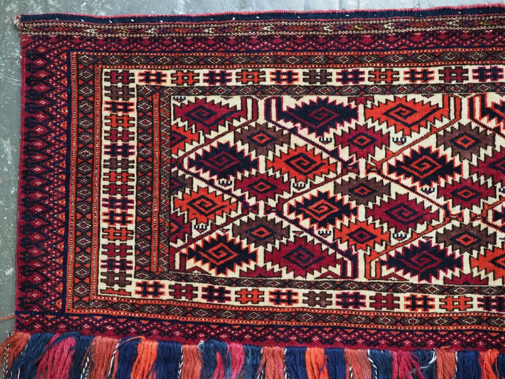 An antique rectangular Tekke Turkmen woven torba face featuring a geometric diamond lattice pattern in burgundy, cream, and orange, finished with long polychrome wool fringes along the lower edge. View III