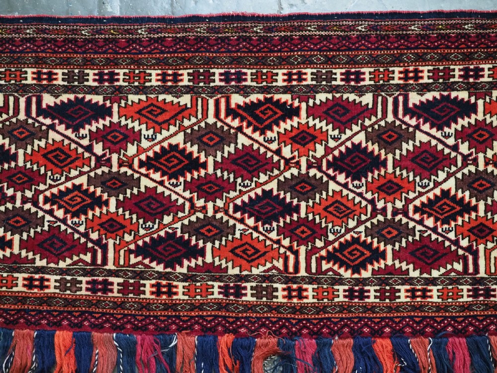 An antique rectangular Tekke Turkmen woven torba face featuring a geometric diamond lattice pattern in burgundy, cream, and orange, finished with long polychrome wool fringes along the lower edge. View IV