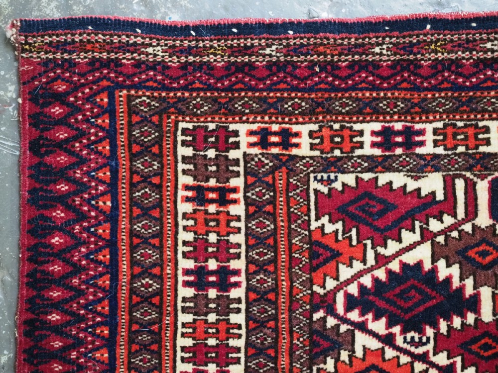 An antique rectangular Tekke Turkmen woven torba face featuring a geometric diamond lattice pattern in burgundy, cream, and orange, finished with long polychrome wool fringes along the lower edge. View VI