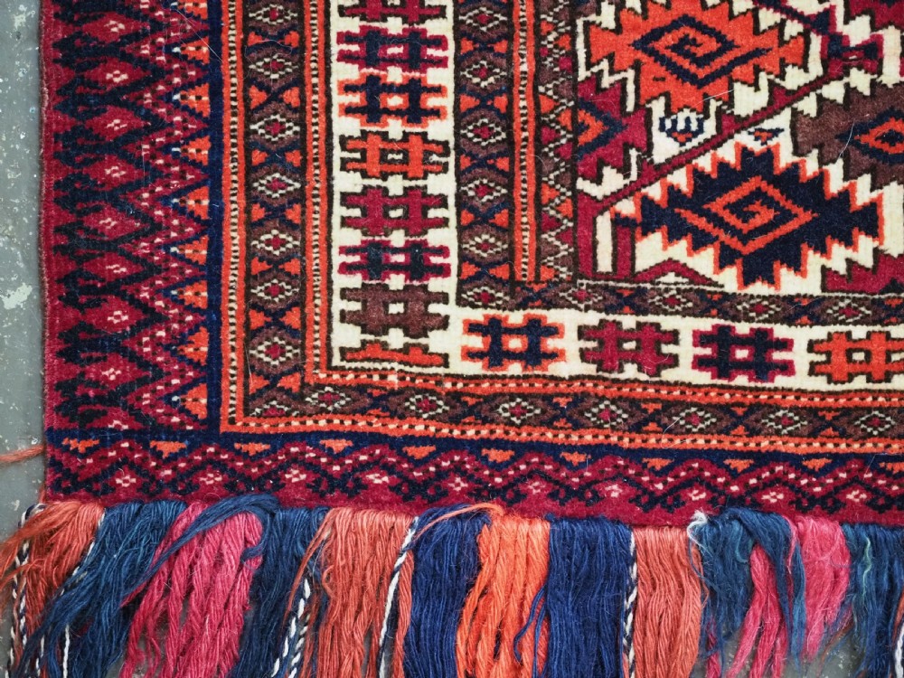 An antique rectangular Tekke Turkmen woven torba face featuring a geometric diamond lattice pattern in burgundy, cream, and orange, finished with long polychrome wool fringes along the lower edge. View VII