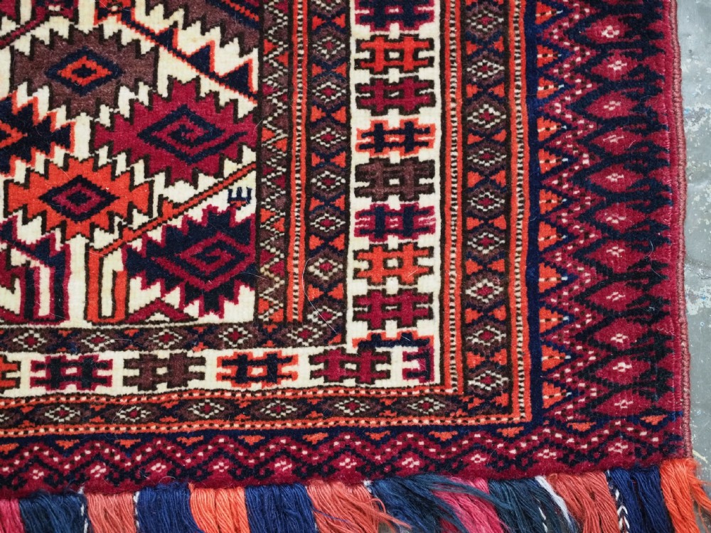 An antique rectangular Tekke Turkmen woven torba face featuring a geometric diamond lattice pattern in burgundy, cream, and orange, finished with long polychrome wool fringes along the lower edge. View X