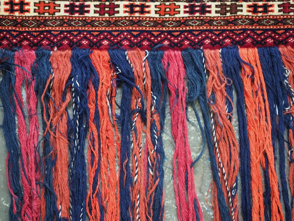 An antique rectangular Tekke Turkmen woven torba face featuring a geometric diamond lattice pattern in burgundy, cream, and orange, finished with long polychrome wool fringes along the lower edge. View XI