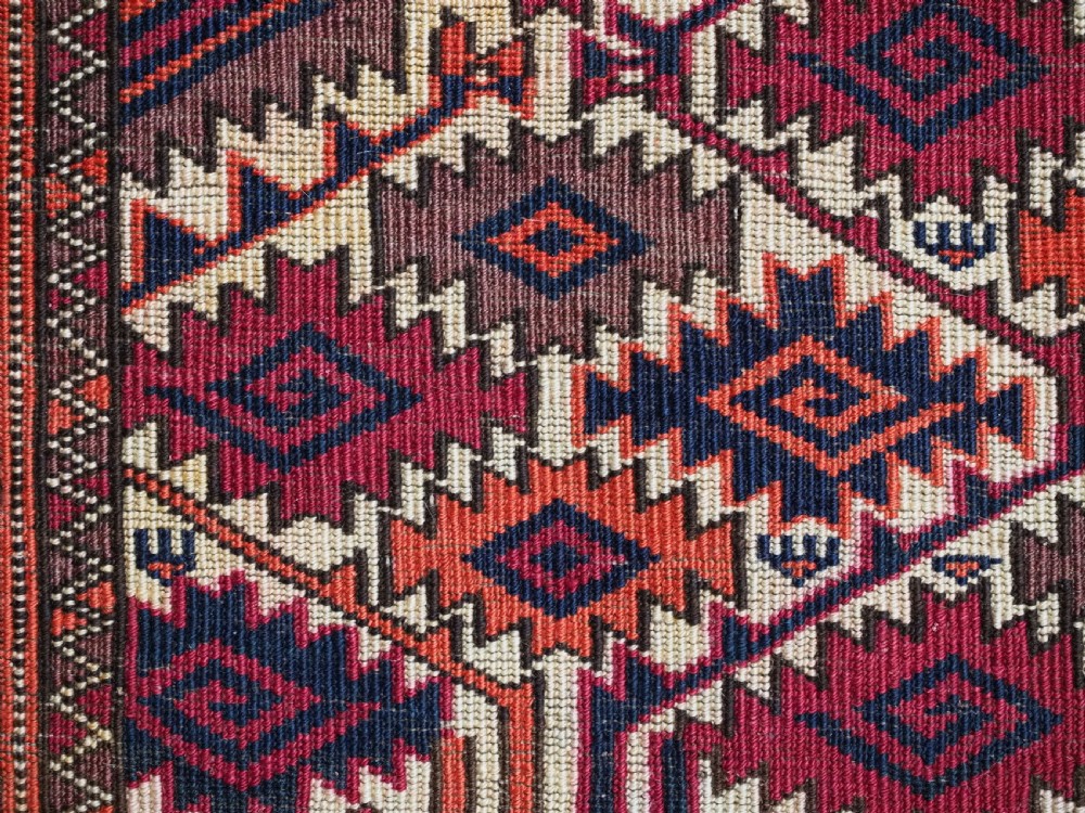 An antique rectangular Tekke Turkmen woven torba face featuring a geometric diamond lattice pattern in burgundy, cream, and orange, finished with long polychrome wool fringes along the lower edge. View XII