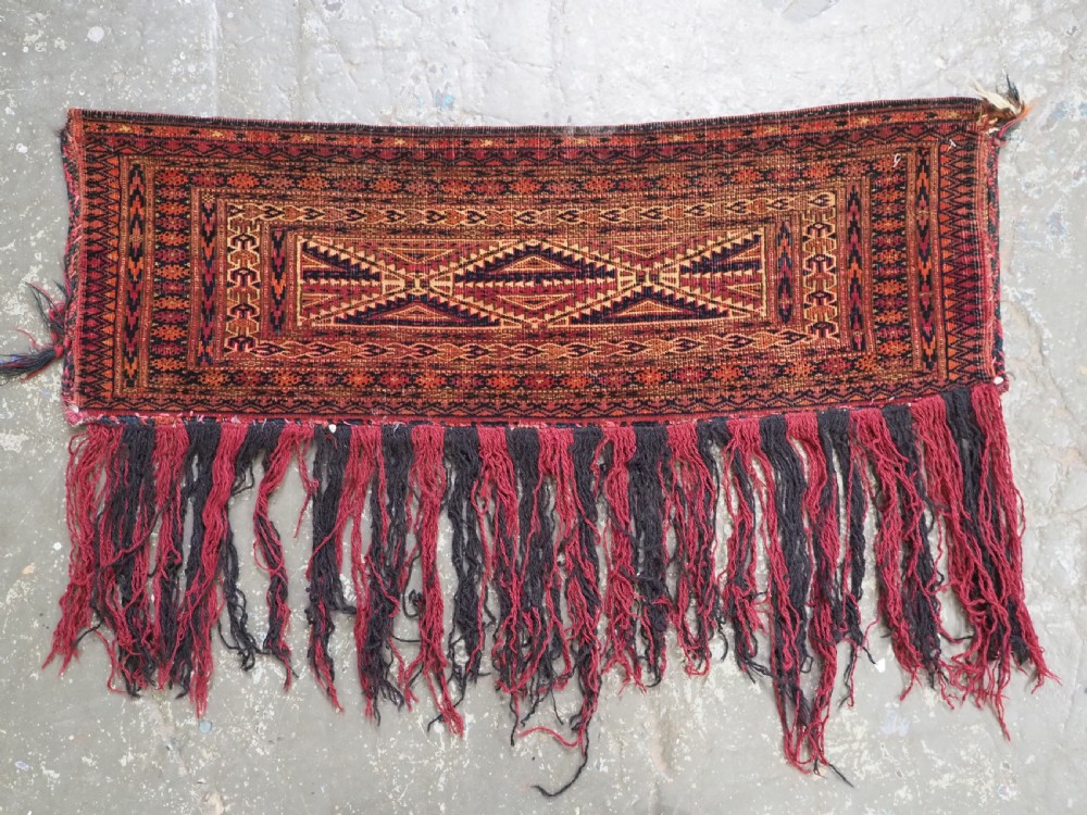 An antique woven Tekke Turkmen torba featuring intricate geometric lattice motifs in dark red, terracotta, and dark blue with a long braided fringe along the bottom edge. View II