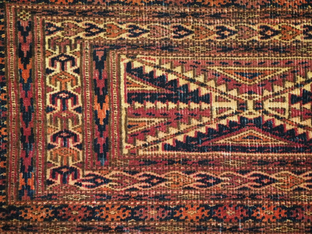 An antique woven Tekke Turkmen torba featuring intricate geometric lattice motifs in dark red, terracotta, and dark blue with a long braided fringe along the bottom edge. View VII