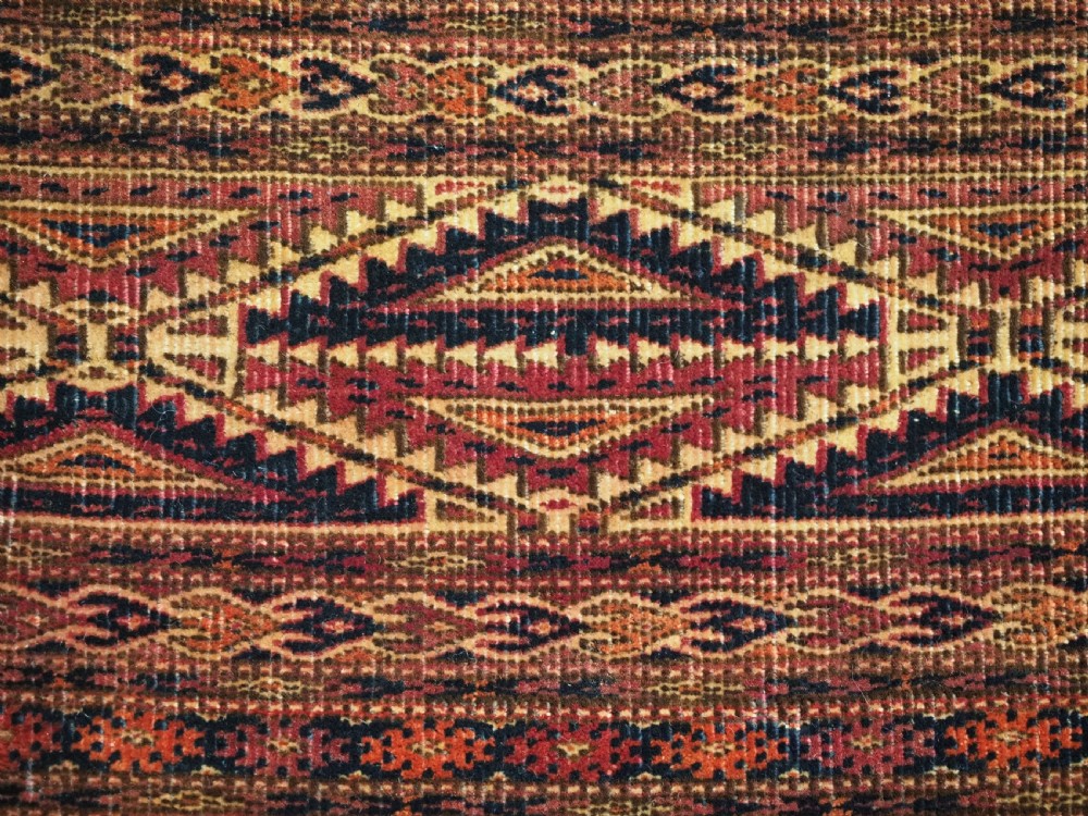 An antique woven Tekke Turkmen torba featuring intricate geometric lattice motifs in dark red, terracotta, and dark blue with a long braided fringe along the bottom edge. View VIII