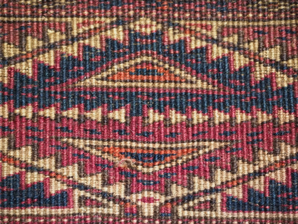 An antique woven Tekke Turkmen torba featuring intricate geometric lattice motifs in dark red, terracotta, and dark blue with a long braided fringe along the bottom edge. View XI