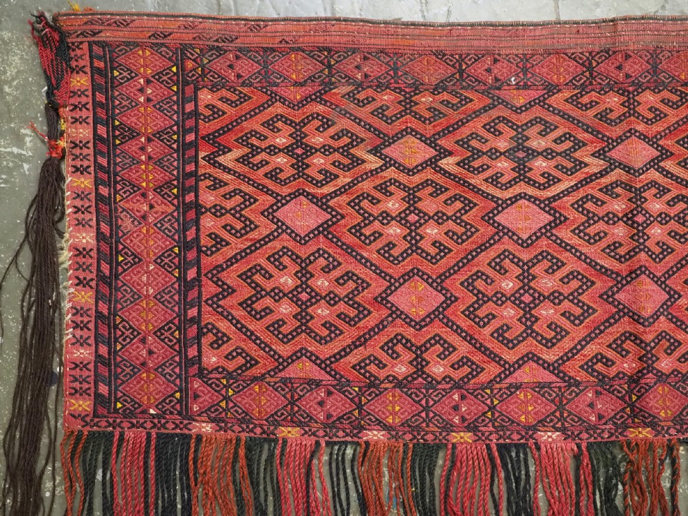 An elongated rectangular Turkmen Ersari torba featuring geometric diamond embroidery in red and dark tones with long fringed tassels along the bottom. View III
