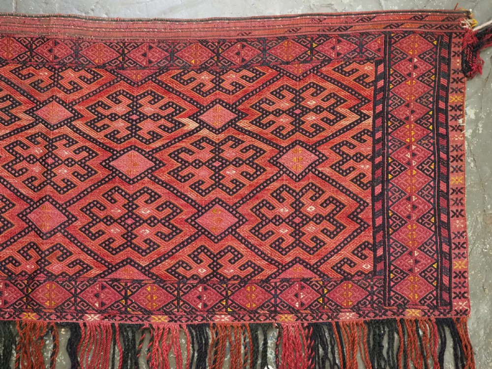 An elongated rectangular Turkmen Ersari torba featuring geometric diamond embroidery in red and dark tones with long fringed tassels along the bottom. View IV