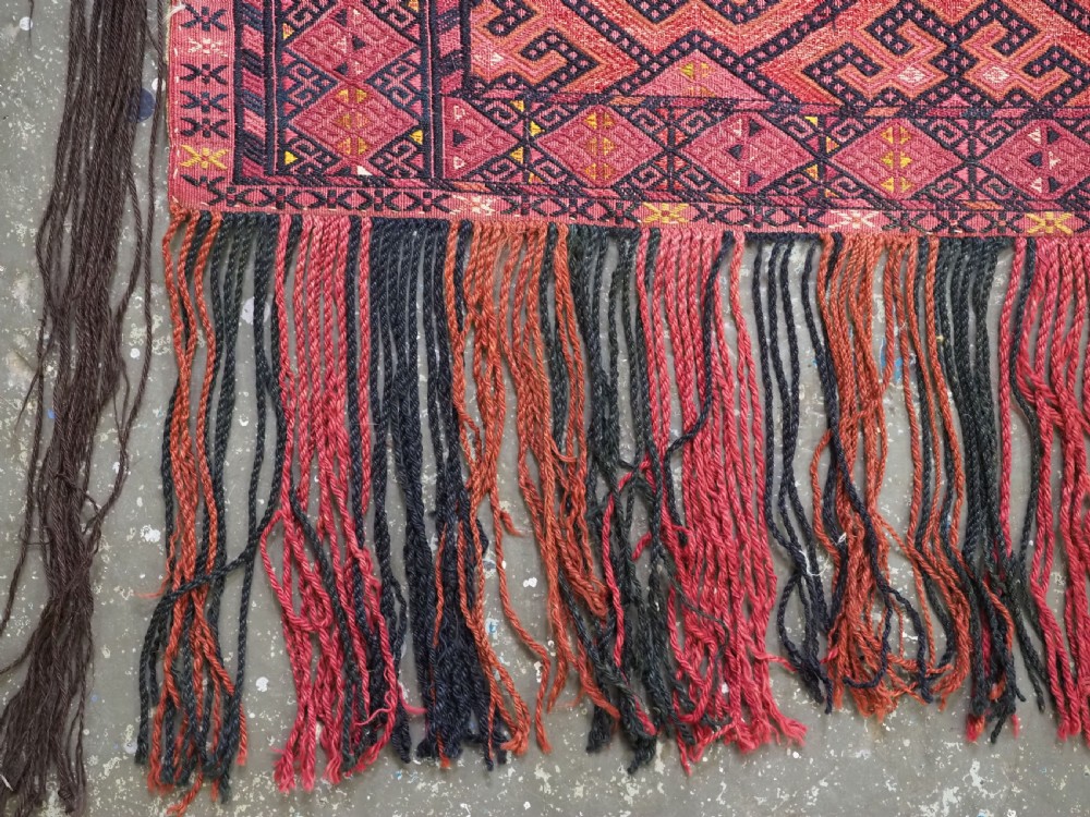 An elongated rectangular Turkmen Ersari torba featuring geometric diamond embroidery in red and dark tones with long fringed tassels along the bottom. View VI