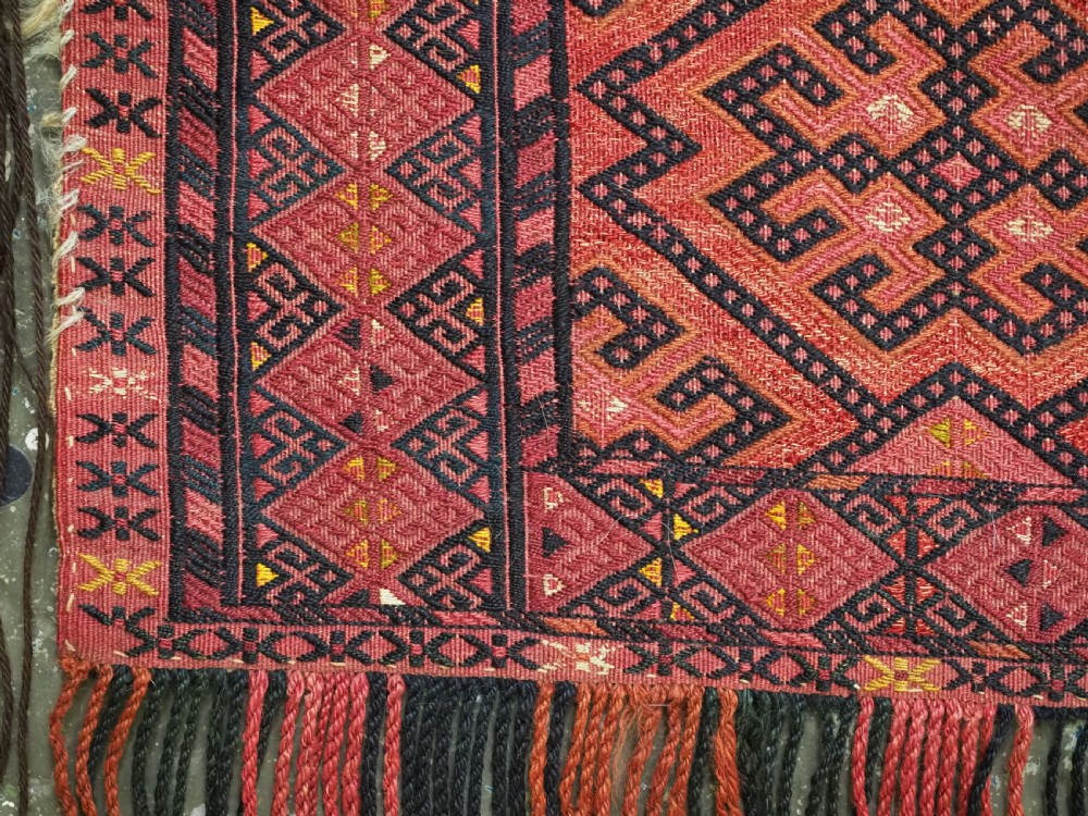An elongated rectangular Turkmen Ersari torba featuring geometric diamond embroidery in red and dark tones with long fringed tassels along the bottom. View VII