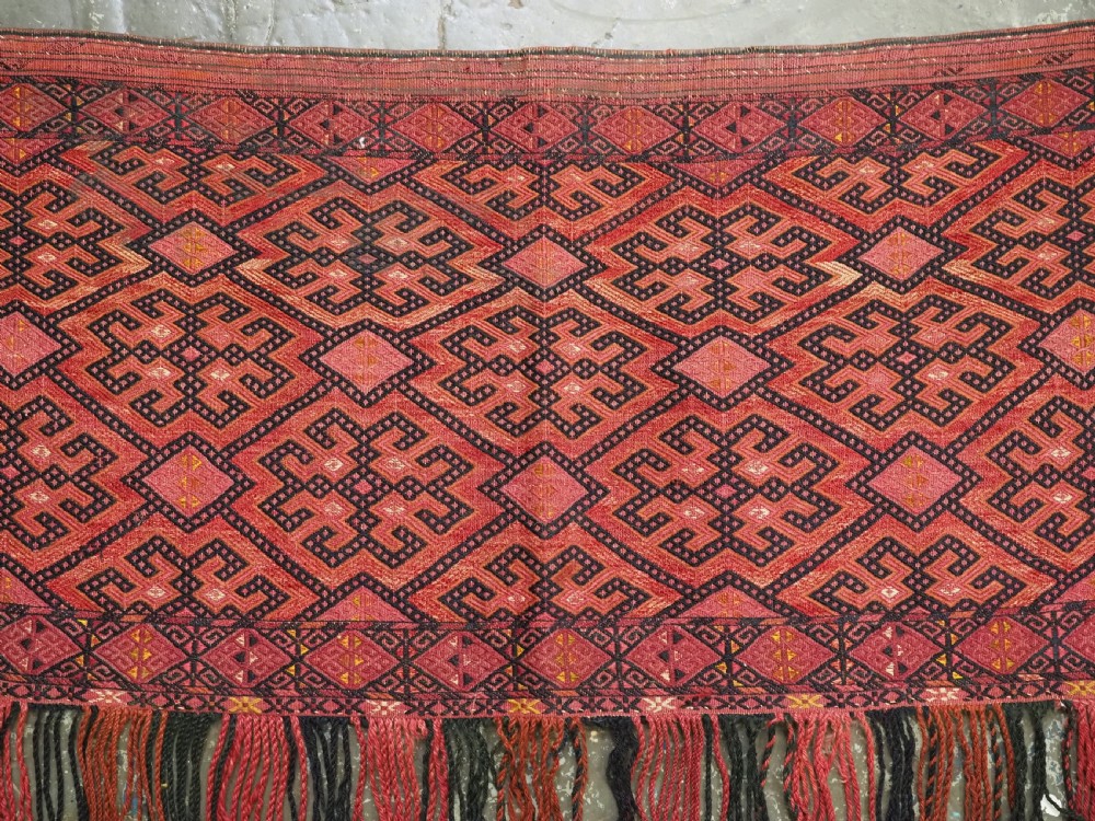 An elongated rectangular Turkmen Ersari torba featuring geometric diamond embroidery in red and dark tones with long fringed tassels along the bottom. View VIII
