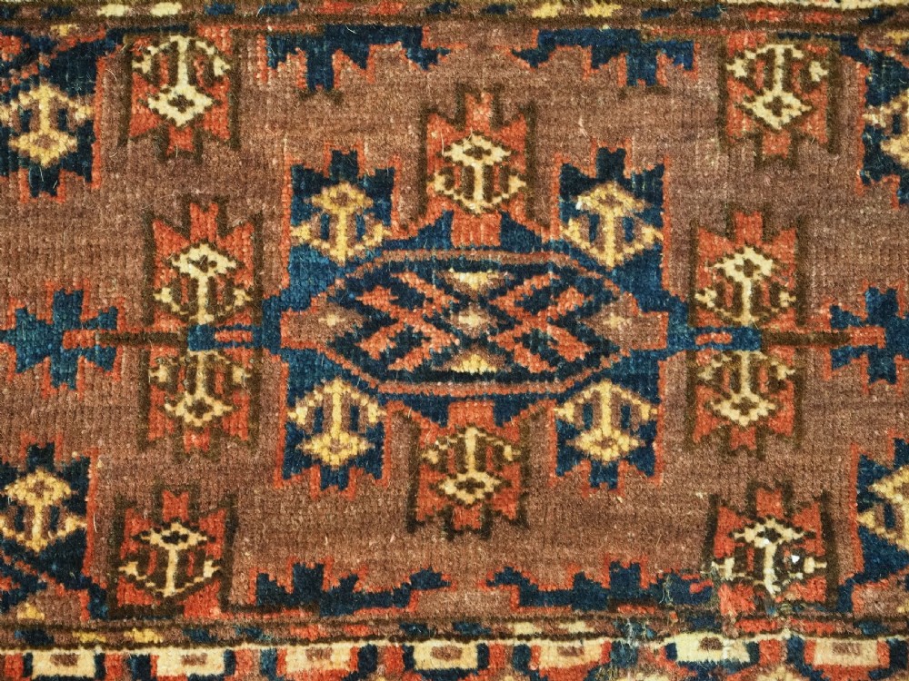 A horizontal rectangular antique wool torba bag face featuring central diamond-shaped Kepse gul motifs in deep red, indigo blue, and ivory framed by a geometric border. View V