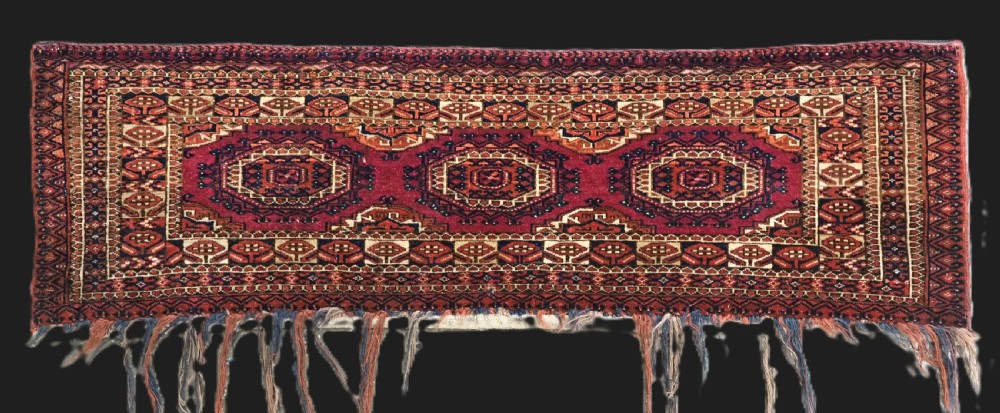 An antique rectangular Tekke Turkmen torba face featuring three central octagonal Salor guls on a deep red wool field with geometric borders and lower fringe.