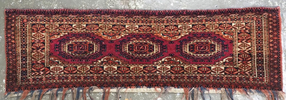 An antique rectangular Tekke Turkmen torba face featuring three central octagonal Salor guls on a deep red wool field with geometric borders and lower fringe. View II