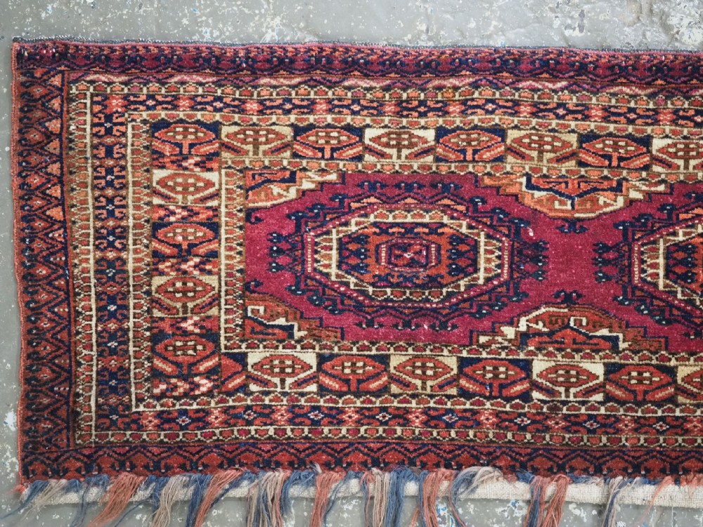 An antique rectangular Tekke Turkmen torba face featuring three central octagonal Salor guls on a deep red wool field with geometric borders and lower fringe. View III