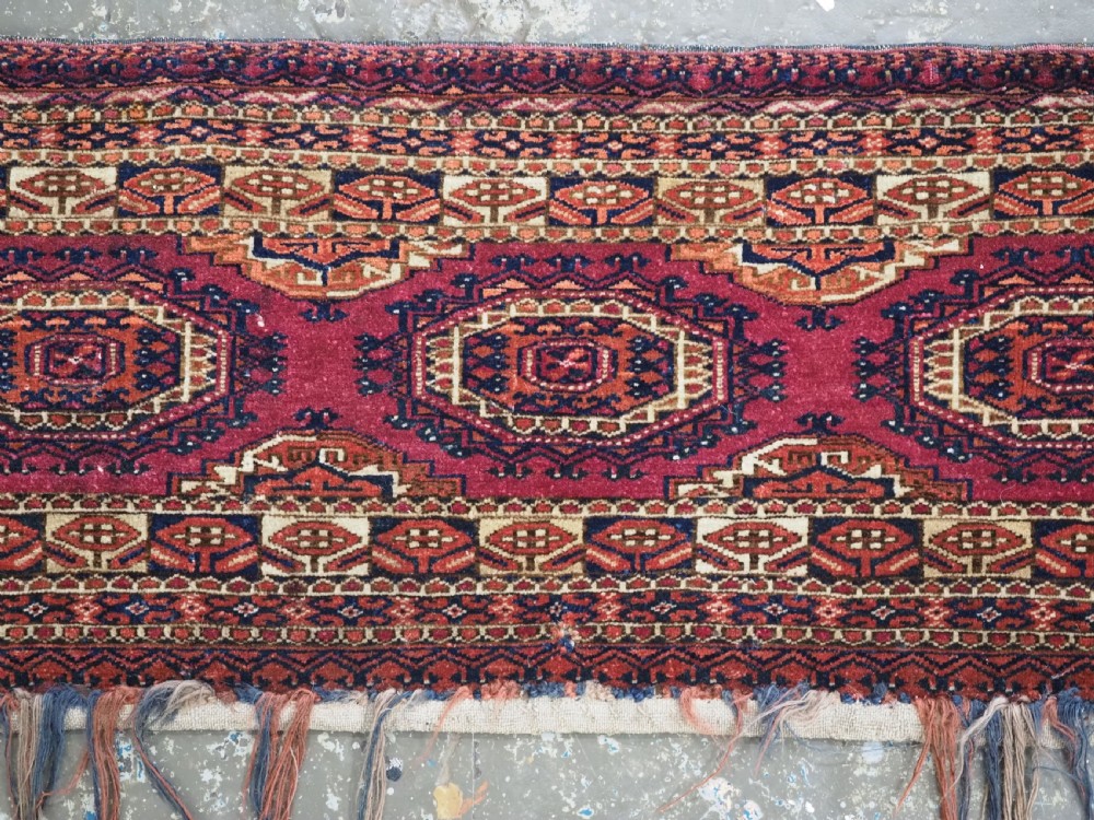 An antique rectangular Tekke Turkmen torba face featuring three central octagonal Salor guls on a deep red wool field with geometric borders and lower fringe. View IV