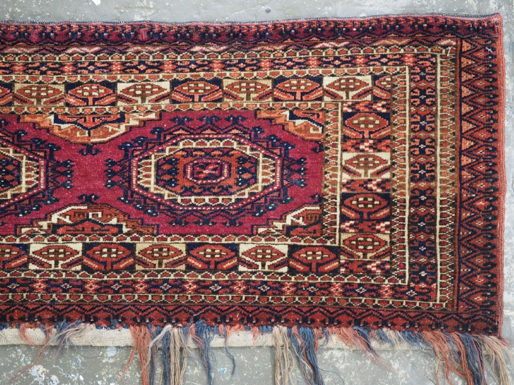 An antique rectangular Tekke Turkmen torba face featuring three central octagonal Salor guls on a deep red wool field with geometric borders and lower fringe. View V