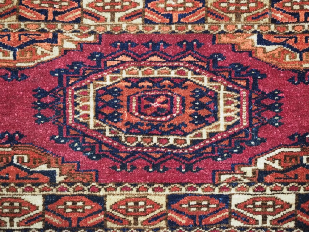 An antique rectangular Tekke Turkmen torba face featuring three central octagonal Salor guls on a deep red wool field with geometric borders and lower fringe. View IX