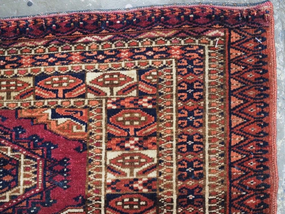 An antique rectangular Tekke Turkmen torba face featuring three central octagonal Salor guls on a deep red wool field with geometric borders and lower fringe. View X