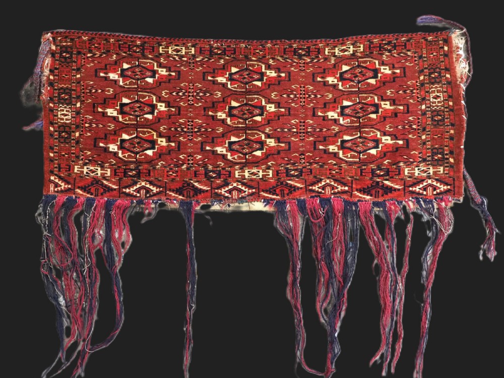 A horizontal rectangular handwoven wool Tekke Turkmen torba bag featuring nine geometric gul motifs in red, navy, and ivory, complete with a long hanging wool fringe at the base.
