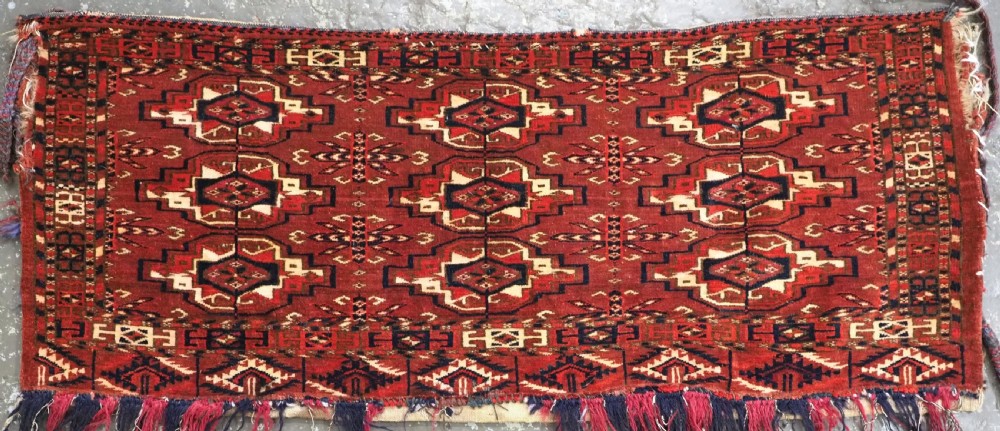 A horizontal rectangular handwoven wool Tekke Turkmen torba bag featuring nine geometric gul motifs in red, navy, and ivory, complete with a long hanging wool fringe at the base. View II