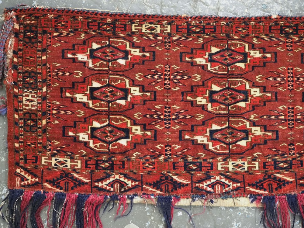 A horizontal rectangular handwoven wool Tekke Turkmen torba bag featuring nine geometric gul motifs in red, navy, and ivory, complete with a long hanging wool fringe at the base. View IV