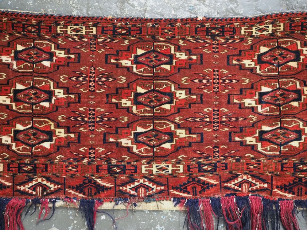 A horizontal rectangular handwoven wool Tekke Turkmen torba bag featuring nine geometric gul motifs in red, navy, and ivory, complete with a long hanging wool fringe at the base. View V
