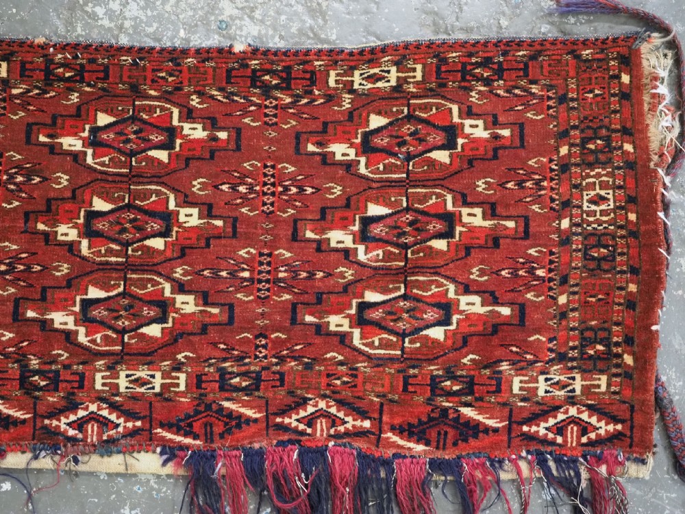 A horizontal rectangular handwoven wool Tekke Turkmen torba bag featuring nine geometric gul motifs in red, navy, and ivory, complete with a long hanging wool fringe at the base. View VI