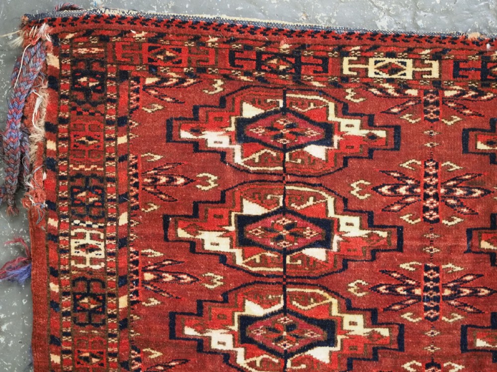A horizontal rectangular handwoven wool Tekke Turkmen torba bag featuring nine geometric gul motifs in red, navy, and ivory, complete with a long hanging wool fringe at the base. View VII