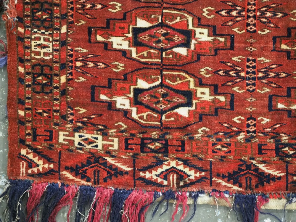 A horizontal rectangular handwoven wool Tekke Turkmen torba bag featuring nine geometric gul motifs in red, navy, and ivory, complete with a long hanging wool fringe at the base. View VIII