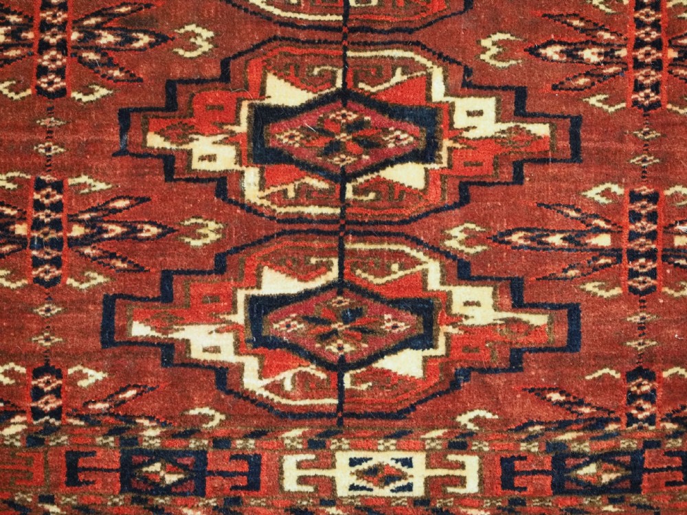 A horizontal rectangular handwoven wool Tekke Turkmen torba bag featuring nine geometric gul motifs in red, navy, and ivory, complete with a long hanging wool fringe at the base. View IX