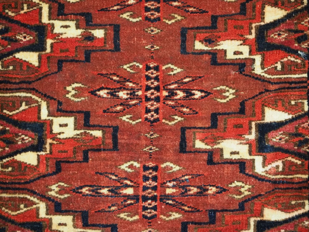A horizontal rectangular handwoven wool Tekke Turkmen torba bag featuring nine geometric gul motifs in red, navy, and ivory, complete with a long hanging wool fringe at the base. View X