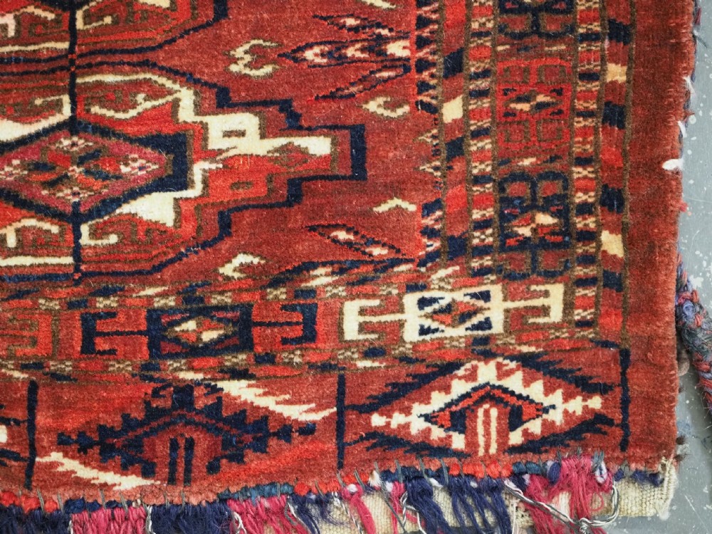 A horizontal rectangular handwoven wool Tekke Turkmen torba bag featuring nine geometric gul motifs in red, navy, and ivory, complete with a long hanging wool fringe at the base. View XI