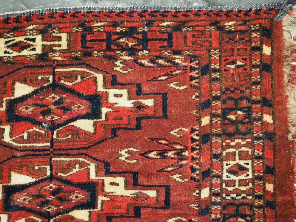 A horizontal rectangular handwoven wool Tekke Turkmen torba bag featuring nine geometric gul motifs in red, navy, and ivory, complete with a long hanging wool fringe at the base. View XII