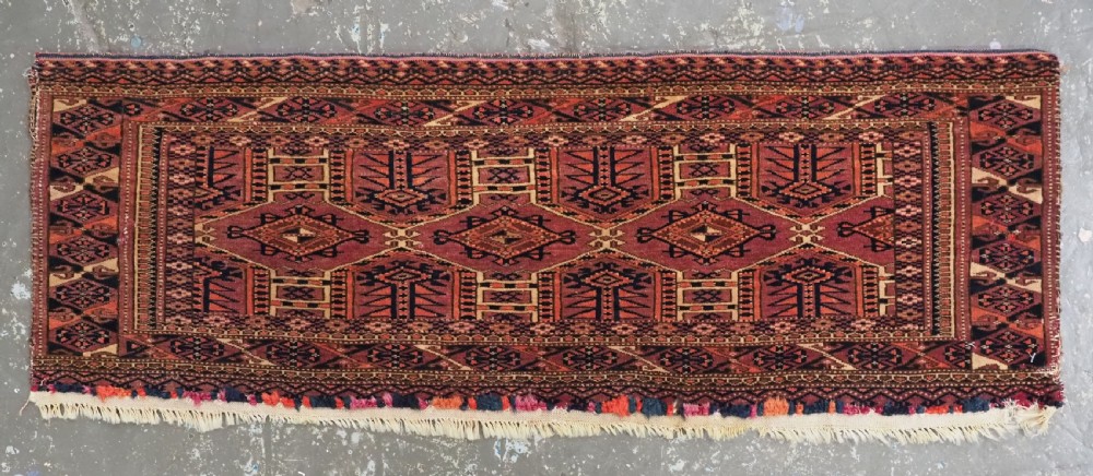 An antique rectangular hand-knotted wool Saryk Turkmen torba face displaying geometric diamond medallions in red, terracotta, and navy shades with lower fringe detail. View II