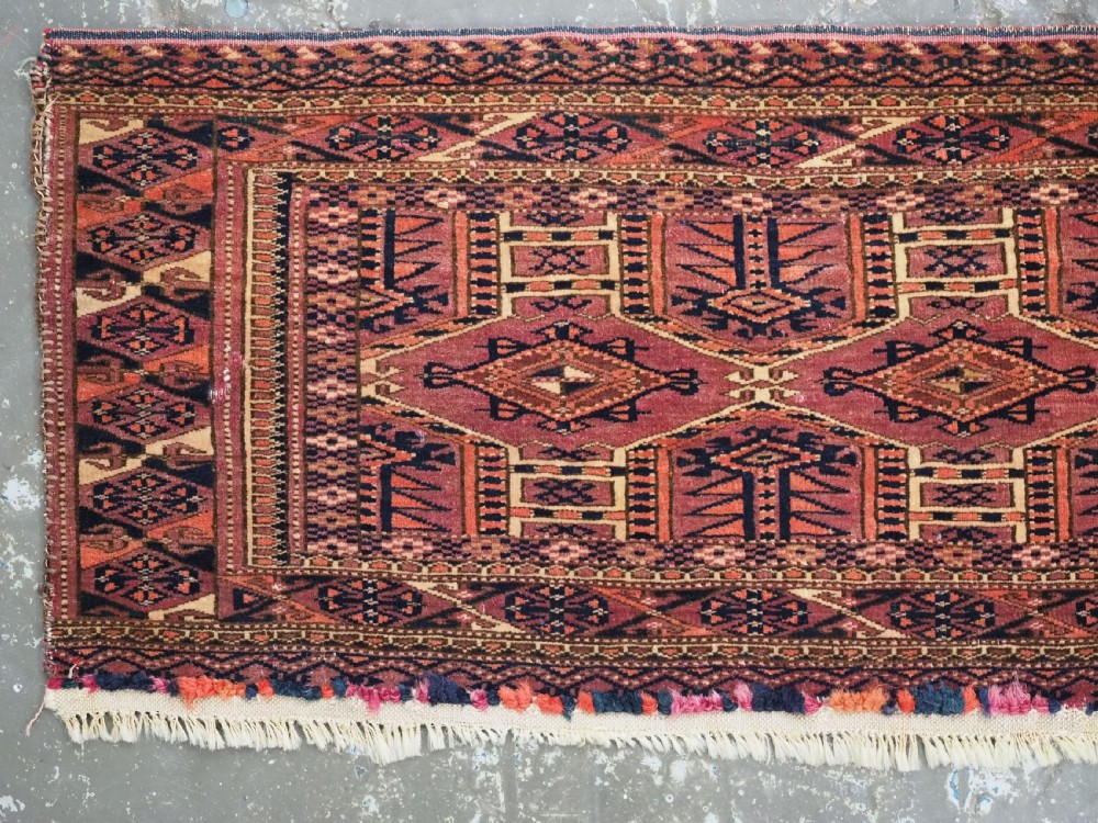 An antique rectangular hand-knotted wool Saryk Turkmen torba face displaying geometric diamond medallions in red, terracotta, and navy shades with lower fringe detail. View III