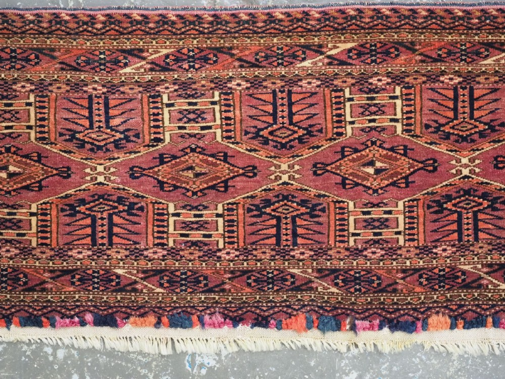 An antique rectangular hand-knotted wool Saryk Turkmen torba face displaying geometric diamond medallions in red, terracotta, and navy shades with lower fringe detail. View IV