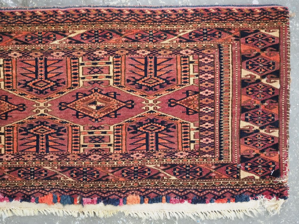 An antique rectangular hand-knotted wool Saryk Turkmen torba face displaying geometric diamond medallions in red, terracotta, and navy shades with lower fringe detail. View V