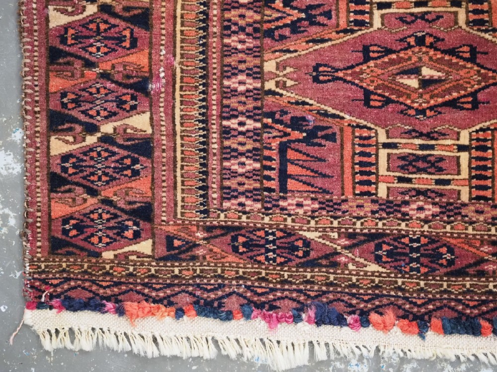 An antique rectangular hand-knotted wool Saryk Turkmen torba face displaying geometric diamond medallions in red, terracotta, and navy shades with lower fringe detail. View VII