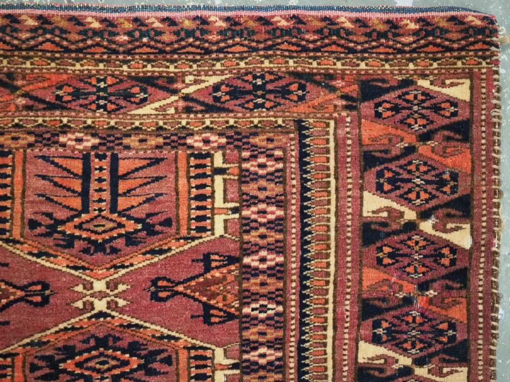 An antique rectangular hand-knotted wool Saryk Turkmen torba face displaying geometric diamond medallions in red, terracotta, and navy shades with lower fringe detail. View X