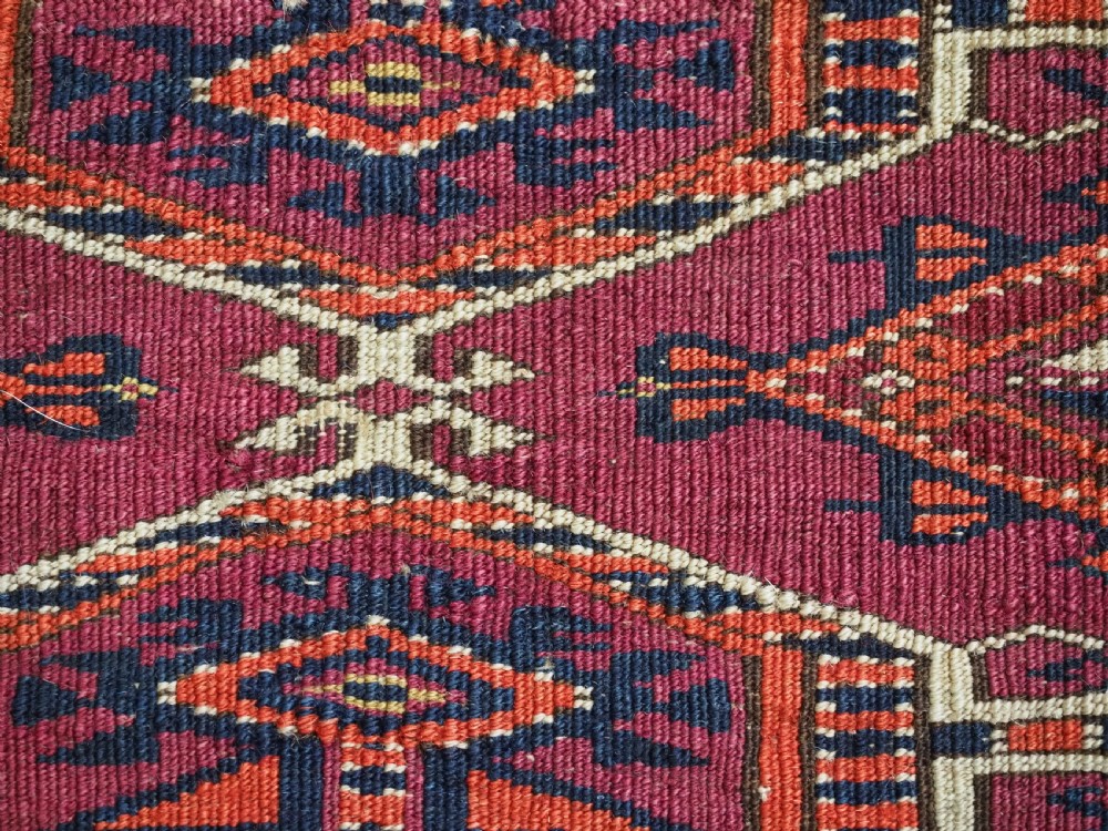 An antique rectangular hand-knotted wool Saryk Turkmen torba face displaying geometric diamond medallions in red, terracotta, and navy shades with lower fringe detail. View XII