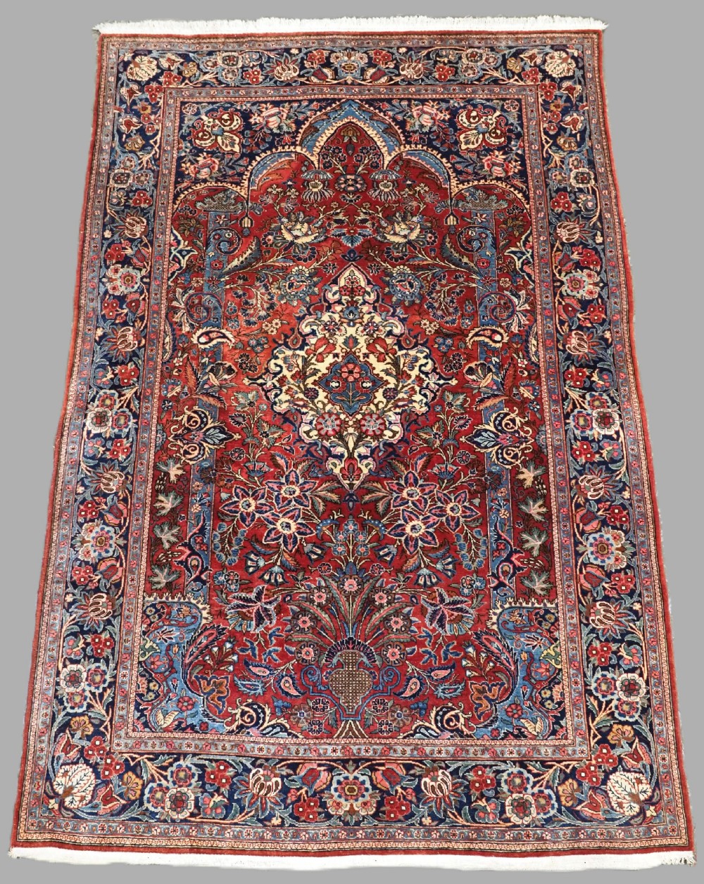 A hand-knotted wool Kashan prayer rug featuring a central floral medallion, a mihrab arch design, and intricate botanical borders in red, navy blue, and cream hues.
