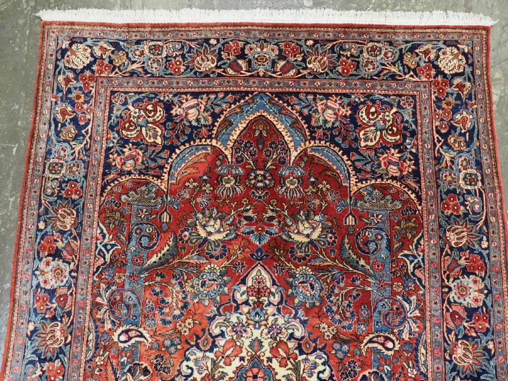 A hand-knotted wool Kashan prayer rug featuring a central floral medallion, a mihrab arch design, and intricate botanical borders in red, navy blue, and cream hues. View VII